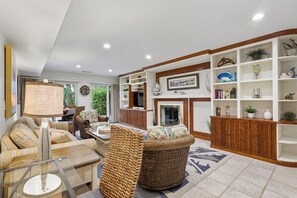 A well-lit living room with a sofa set, a coffee table, and a wicker chair. There is a bookshelf with decorative items and a television. - Gorgeous Villa w/ Panoramic Views (Hilton Head Island)