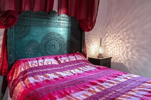 A bed with a patterned bedspread, a decorative headboard, and a bedside lamp.