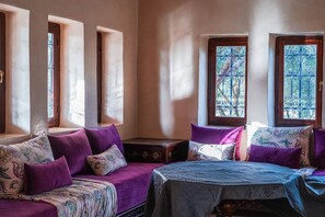 A room with a bed, a sofa, and a small table. There are windows with decorative iron bars.