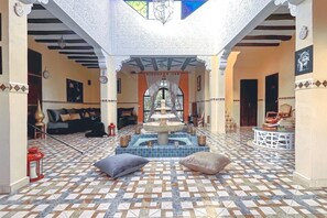 A courtyard with a fountain, tiled floor, seating areas, and a view of the interior.