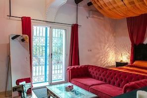 A room with a red sofa, a glass coffee table, a mirror, and a window with red curtains.