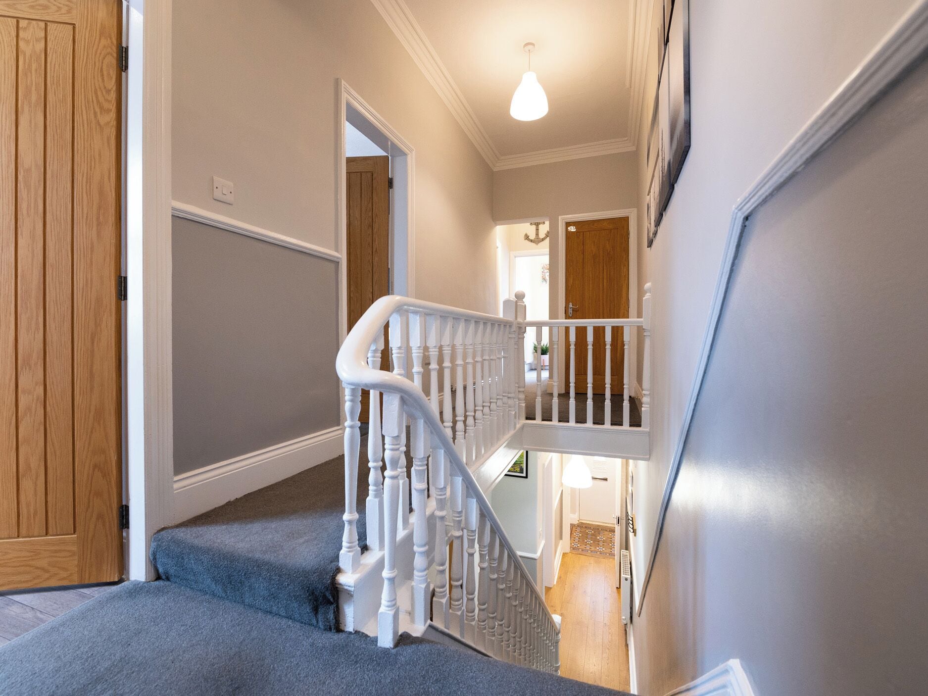 A staircase with white balusters leading to a second floor, a light fixture above, and a door with a wooden frame.