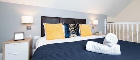 A hotel room with a bed, two bedside tables, a nightstand, a lamp, and a white railing.