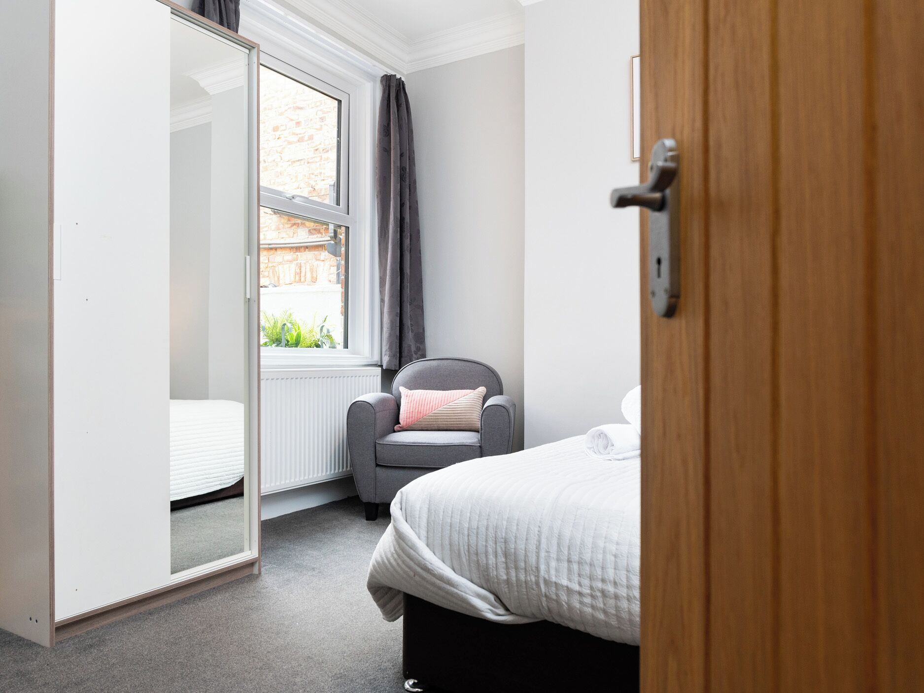 A bedroom with a bed, a chair, a wardrobe, and a window with curtains.
