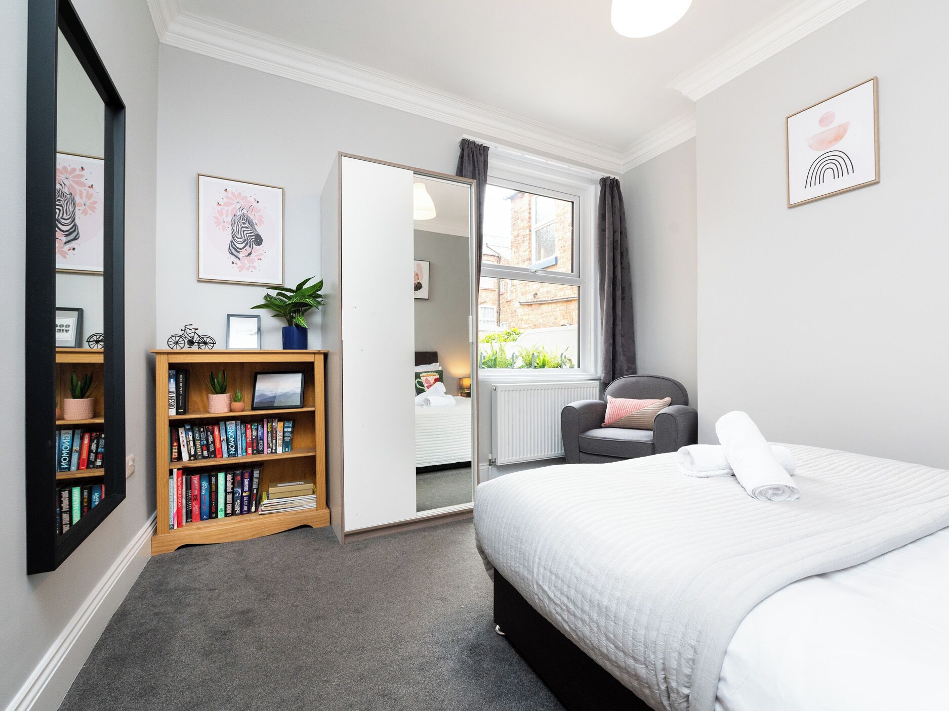 A bedroom with a bed, a bookshelf, a chair, and a window.