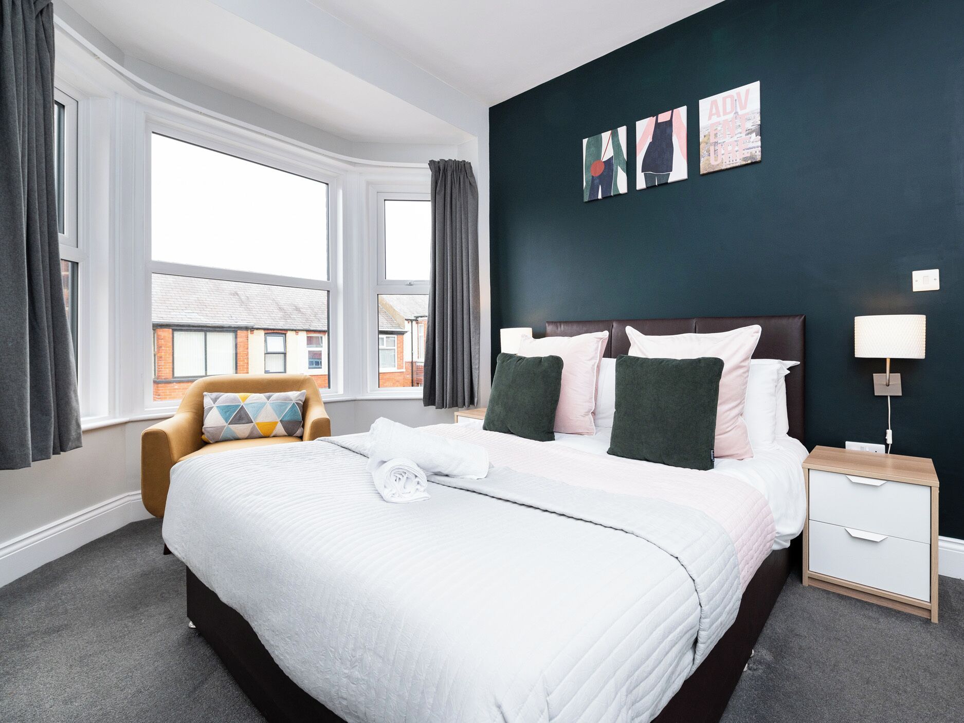 A hotel room with a large bed, a chair, a nightstand, and artwork on the wall.