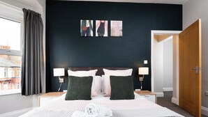 A hotel room with a large bed, two bedside tables, a nightstand, a window with curtains, and a door. - 38 Ashville Avenue (Scarborough)