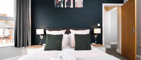 A hotel room with a large bed, two bedside tables, a nightstand, a window with curtains, and a door.