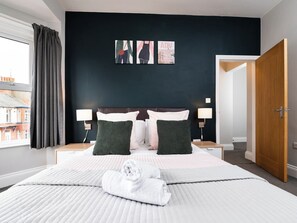A hotel room with a large bed, two bedside tables, a nightstand, a window with curtains, and a door. - 38 Ashville Avenue (Scarborough)