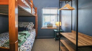 A dormitory room with bunk beds, a desk, a chair, and a window with blinds. - Foxglove Cottage (Conwy)