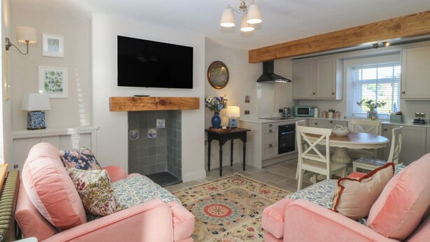 A living room with a fireplace, a television mounted above it, and a dining area with a table and chairs. - Foxglove Cottage (Conwy)
