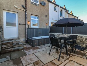 A patio with stone flooring, a seating area with chairs and a table, and a built-in bench with storage. - Foxglove Cottage (Conwy)