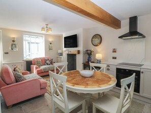 A cozy living room with a pink sofa, a round wooden table, and white chairs. - Foxglove Cottage (Conwy)