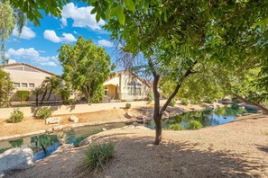 Zona residencial con un pequeño estanque, una casa de techo rojo y un árbol en primer plano.