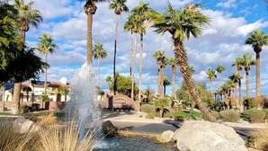 A landscaped area with a fountain, palm trees, and a building with a sign reading 'Litchfield.' - Midterm Retreat in Gated Golf Community (Litchfield Park)
