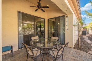 Eine verglaste Terrasse mit einem runden Tisch und Stühlen, einem Deckenventilator und Blick ins Freie.