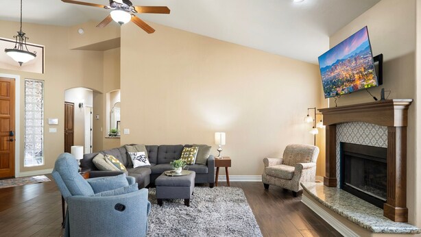 A living room with a fireplace, a television mounted above it, and a ceiling fan. - Midterm Retreat in Gated Golf Community (Litchfield Park)