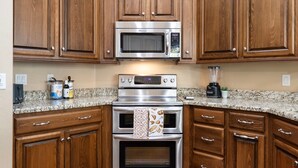A kitchen with wooden cabinets, a stainless steel microwave, an oven, and a blender on the countertop. - Midterm Retreat in Gated Golf Community (Litchfield Park)