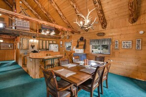 Ein Holzblockhaus-Interieur mit Essbereich, Küche und einer Chandelüster.