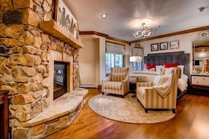 A cozy living room with a stone fireplace, comfortable seating, and a large bed with a headboard. - BC Slopeside Ski Studio, Hot Tub, Resort Amenities (Beaver Creek)