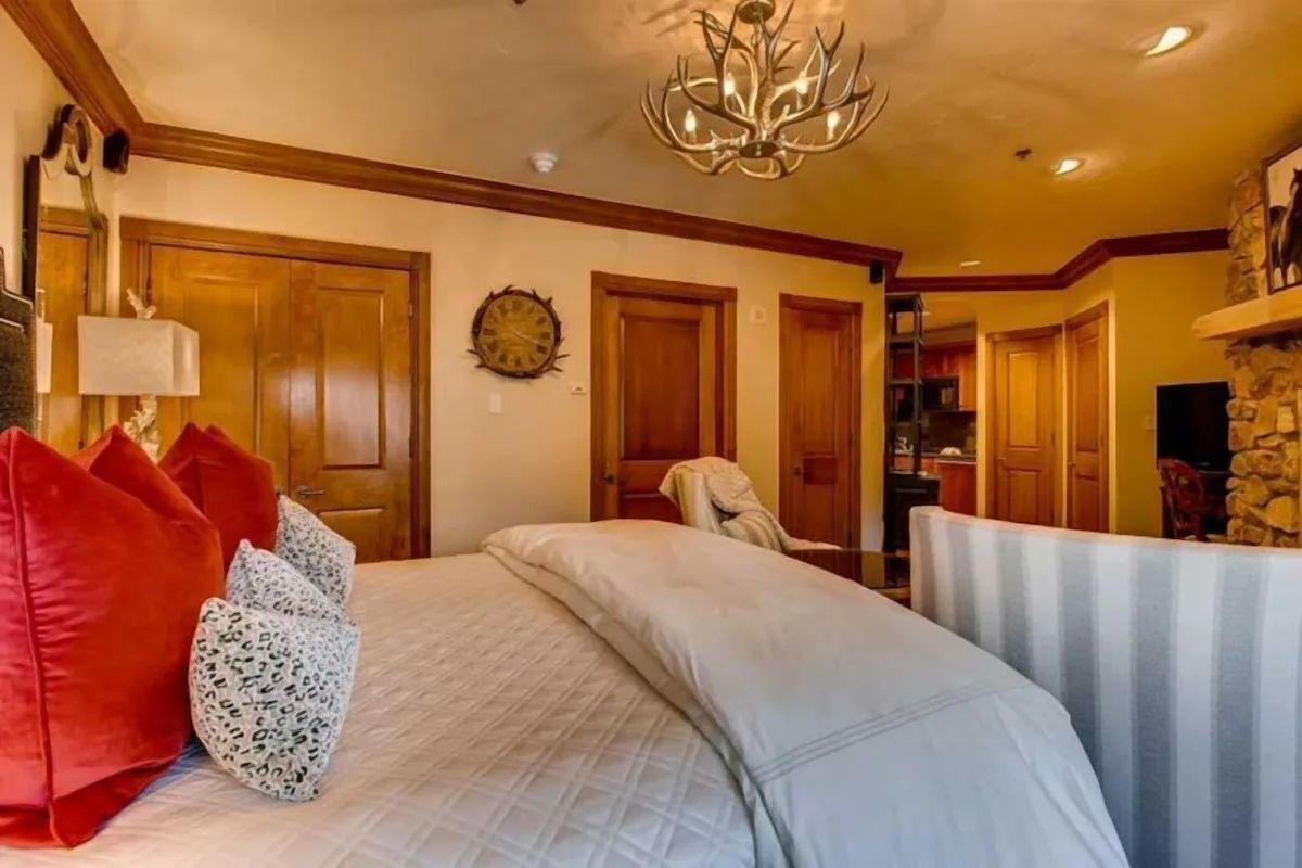 A bedroom with a bed, pillows, a chandelier, wooden doors, and a stone fireplace.