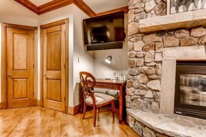 A room with a stone fireplace, wooden doors, a television mounted above it, and a desk with a chair. - BC Slopeside Ski Studio, Hot Tub, Resort Amenities (Beaver Creek)
