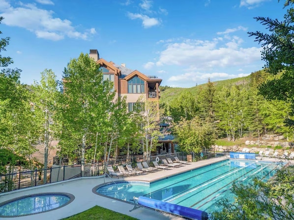 A hotel with a swimming pool, lounge chairs, and a mountainous backdrop. - BC Slopeside Ski Studio, Hot Tub, Resort Amenities (Beaver Creek)