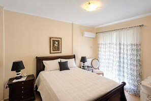 A bedroom with a bed, bedside tables, a lamp, a mirror, a picture on the wall, and a window with curtains. - Escape to our spacious country home. (DIMOS EUROTA)