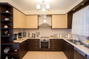 A modern kitchen with dark brown cabinets, a central island, a built-in oven, and a stainless steel sink. - Escape to our spacious country home. (DIMOS EUROTA)