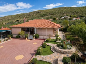 A single-story house with a tiled roof, a covered porch, and a landscaped garden with a stone pathway. - Escape to our spacious country home. (DIMOS EUROTA)