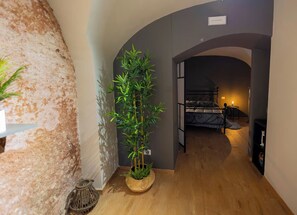 A hallway with a wooden floor, a potted bamboo plant, and a bed in the background. - Lavika Home (Catania)