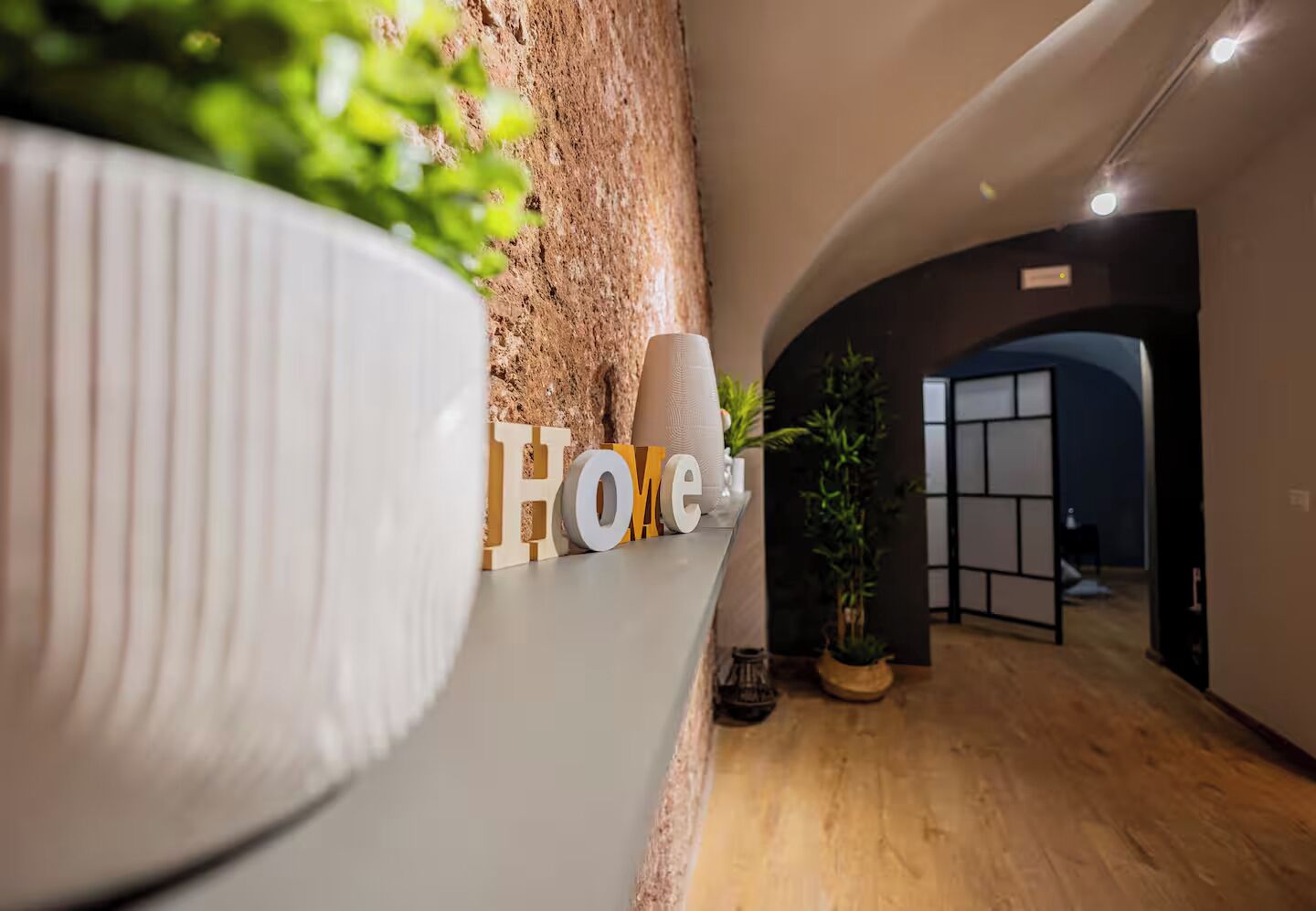 A hallway with a wooden floor, a potted plant, and a wall with the word 'Home' spelled out in letters.