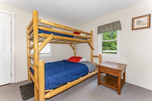 Una cama individual con estructura de madera, una mesita de noche pequeña y una ventana con vistas al verdor.