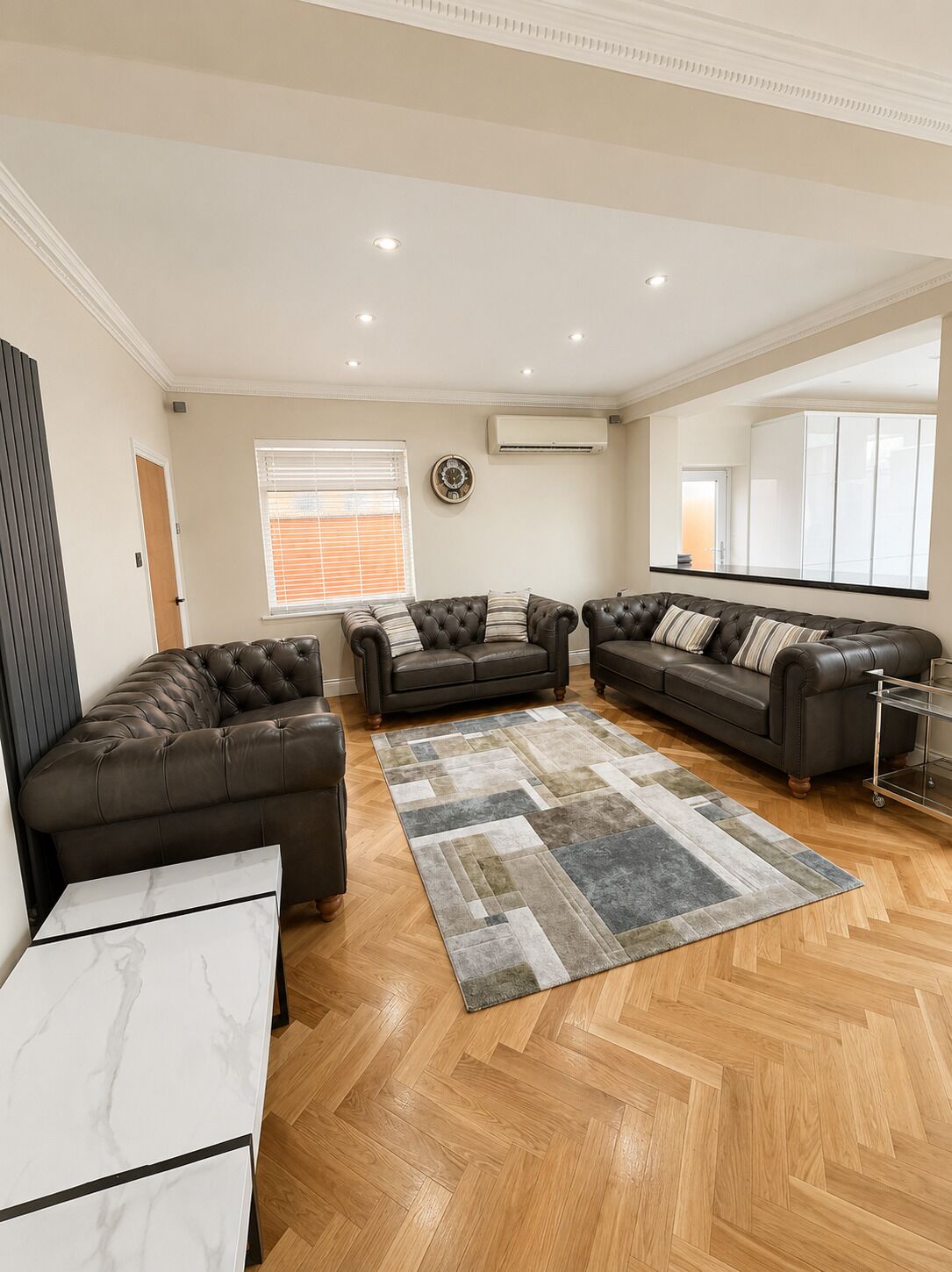 A spacious living room with a large sectional sofa, a marble coffee table, and a herringbone wood floor.