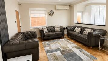 A spacious living room with a large sectional sofa, a marble coffee table, and a herringbone wood floor.