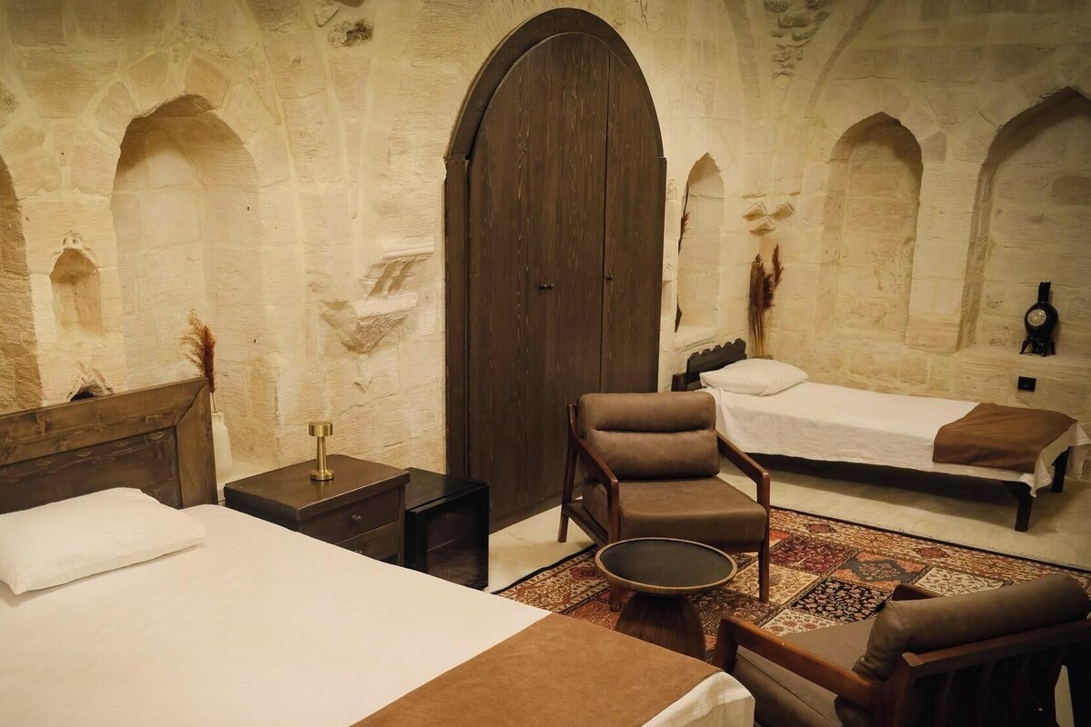 A room with a large bed, a smaller bed, a chair, a nightstand, and a large wooden door.