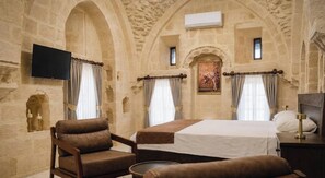 A room with a bed, two chairs, a small table, and a television mounted on the wall. - MİRA KONAĞI  (Mardin)