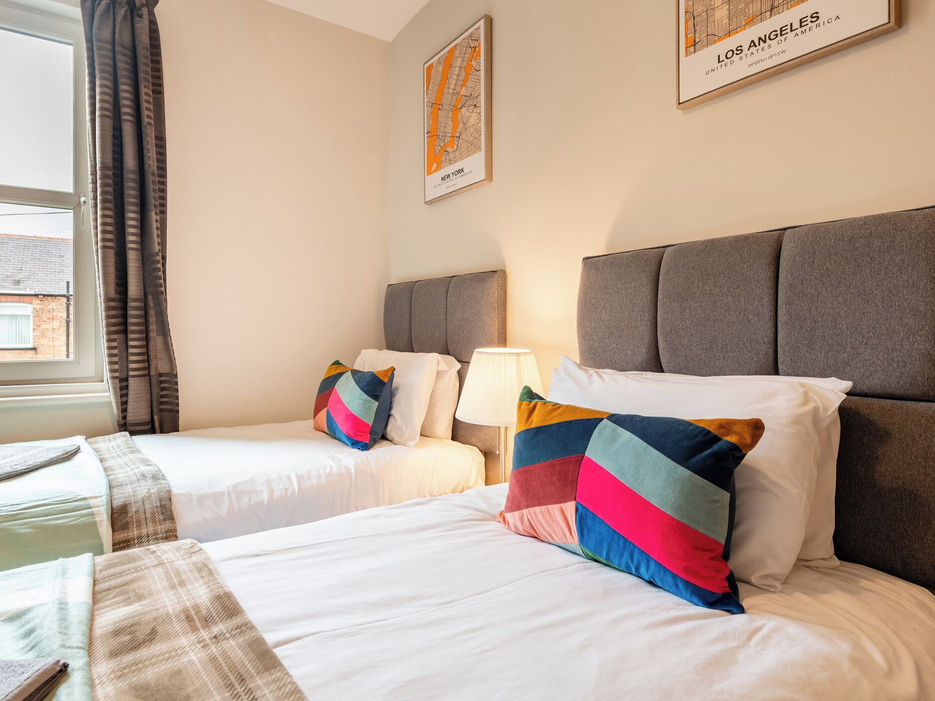 A hotel room with two beds, a window with curtains, a lamp, and a map on the wall.