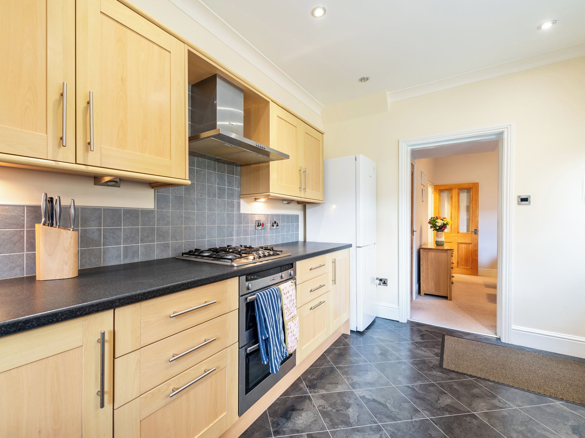 A modern kitchen with wooden cabinets, a black countertop, and a stainless steel range hood.