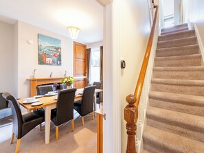 Un coin repas avec une table et des chaises en bois, un tableau au mur et un escalier dont les marches sont recouvertes de moquette.