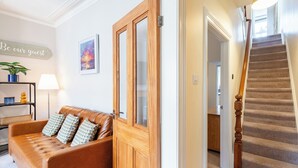 Una sala de estar con un sofá de cuero marrón, una puerta de madera, una escalera y un letrero en la pared.
