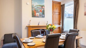 Un comedor con una mesa de madera dispuesta para seis personas, rodeada de sillas, un florero y un cuadro en la pared.