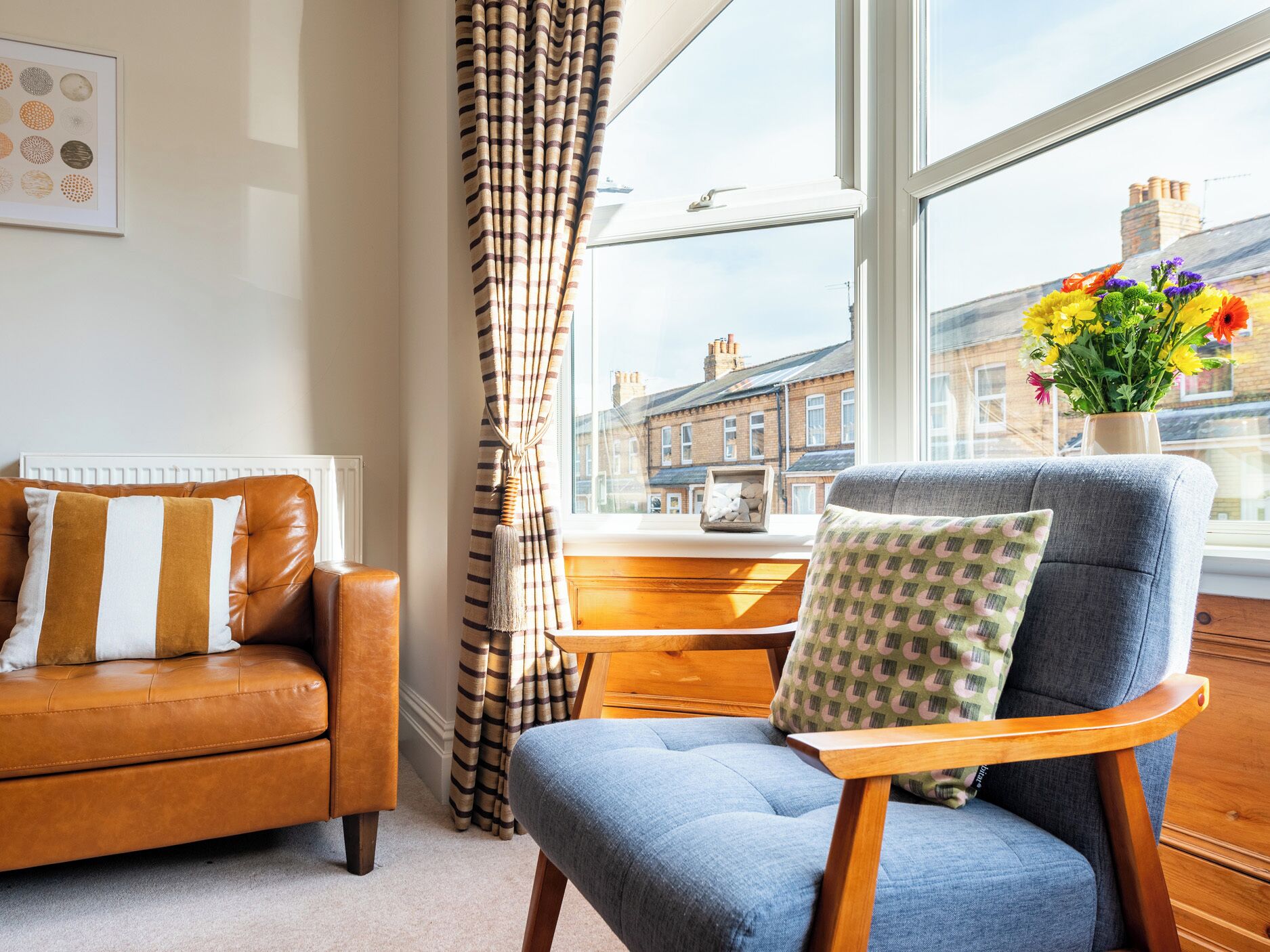 Ein Wohnzimmer mit einer Ledersofa, einem blauen Sessel und Blick auf eine Skyline durch große Fenster.