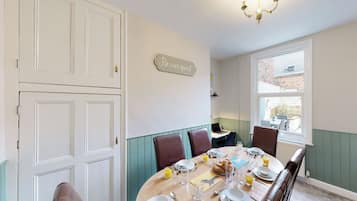 Un coin repas avec une table dressée pour quatre personnes, un lustre et un panneau indiquant : « Soyez nos invités. »