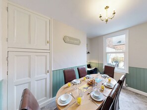 A dining area with a table set for four, a chandelier, and a sign that reads 'Be our guest'. - 44 Norwood Street (Scarborough)