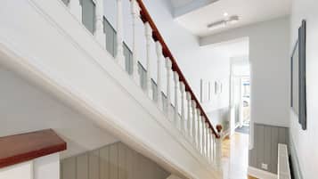 Un escalier avec des balustrades blanches et une main courante en bois, menant à une pièce équipée d’un radiateur et d’une porte donnant sur l’extérieur.