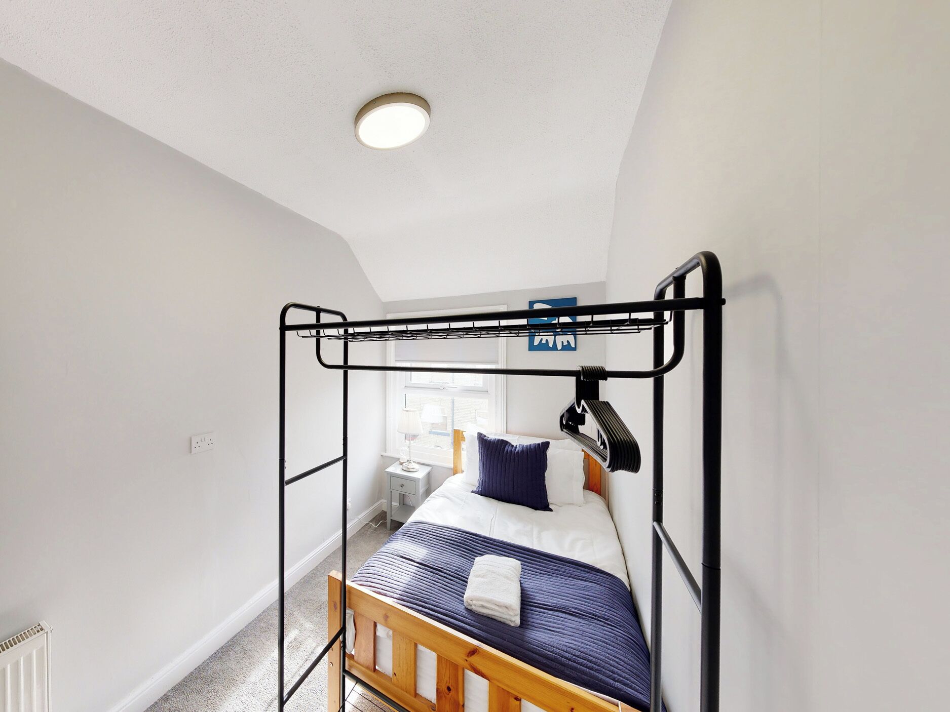 Una cama individual con cabecera, una mesita de noche, una lámpara y una ventana con vistas.