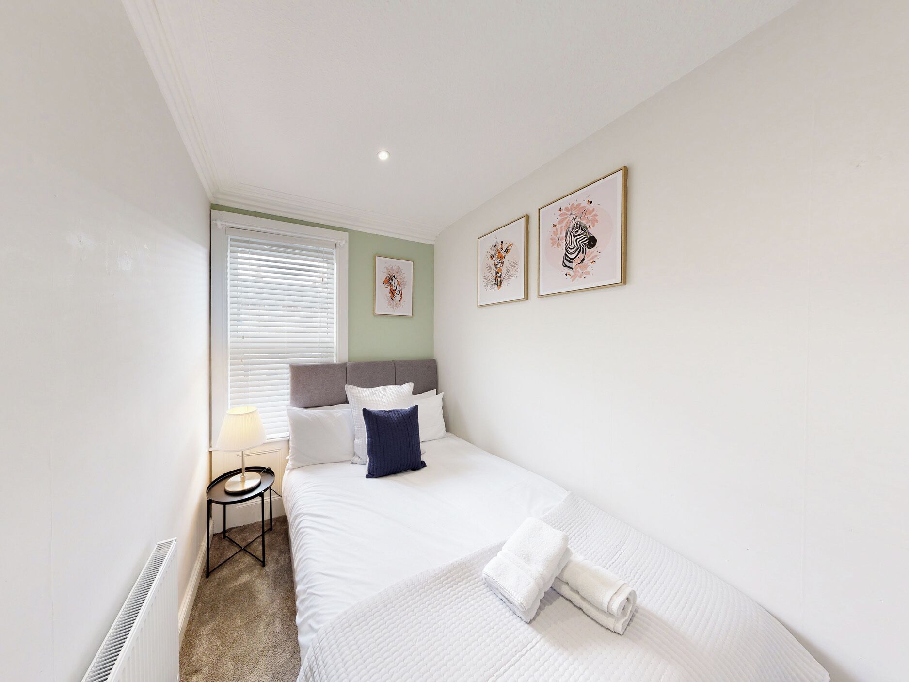 A hotel room with a bed, a bedside table, a lamp, and artwork on the wall.