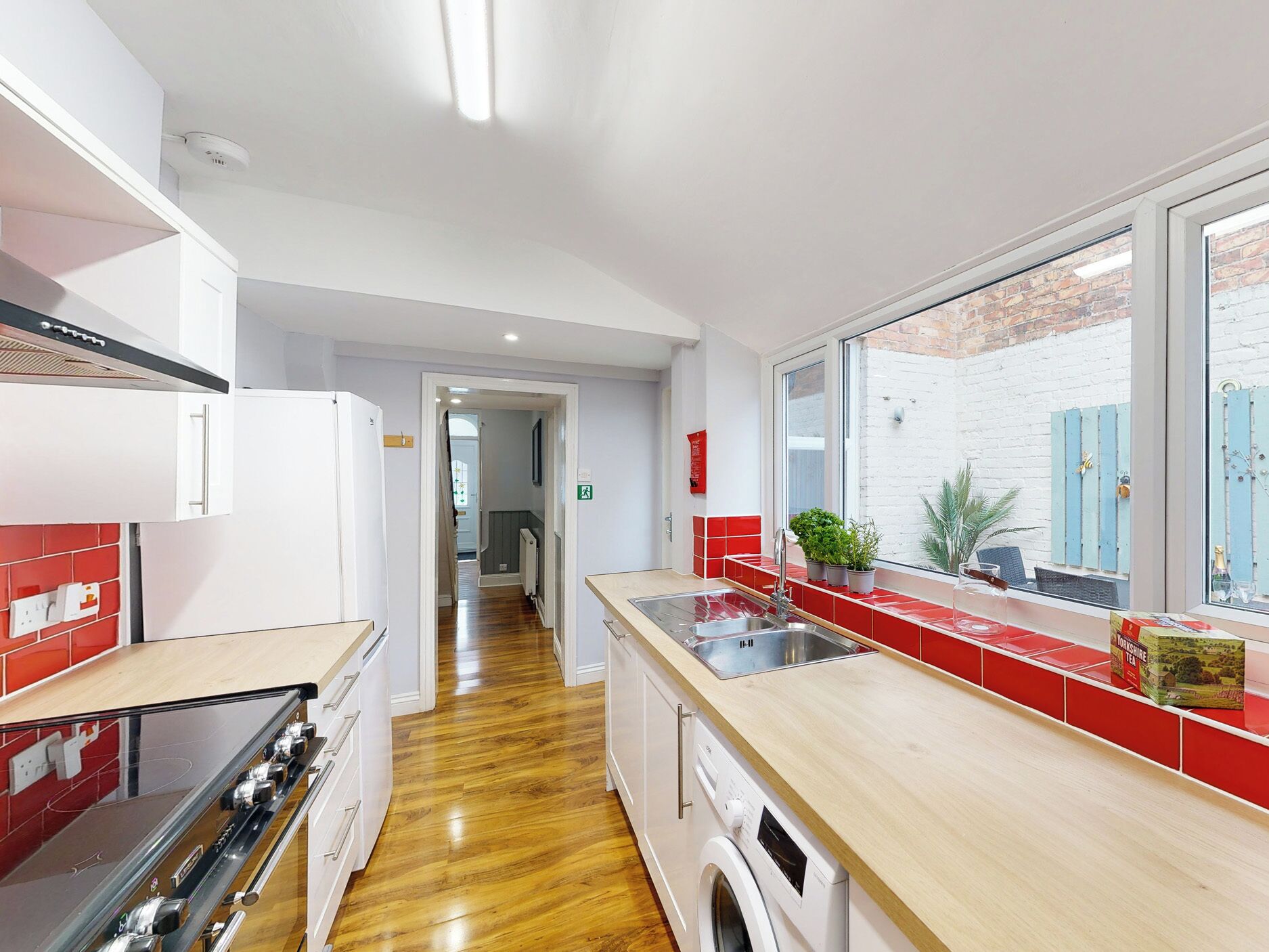 A modern kitchen with a wooden floor, stainless steel appliances, and a red backsplash.