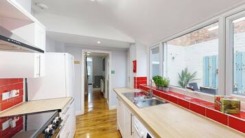 A modern kitchen with a wooden floor, stainless steel appliances, and a red backsplash.